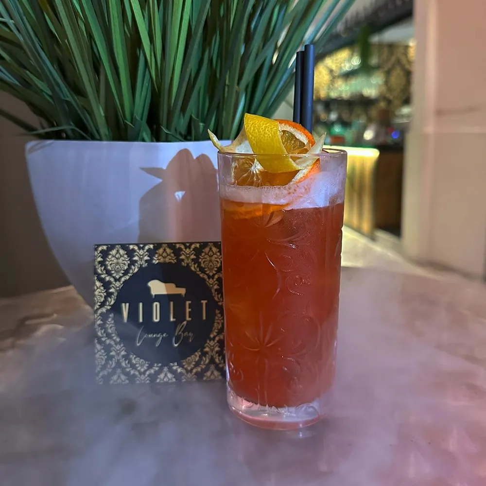 Cocktail rosso accanto al biglietto da visita nero e oro del Violet